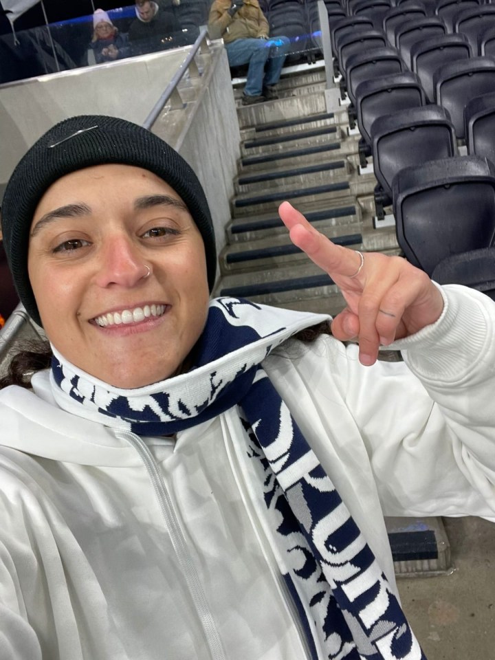 Selfie of a woman at a stadium, giving a peace sign.