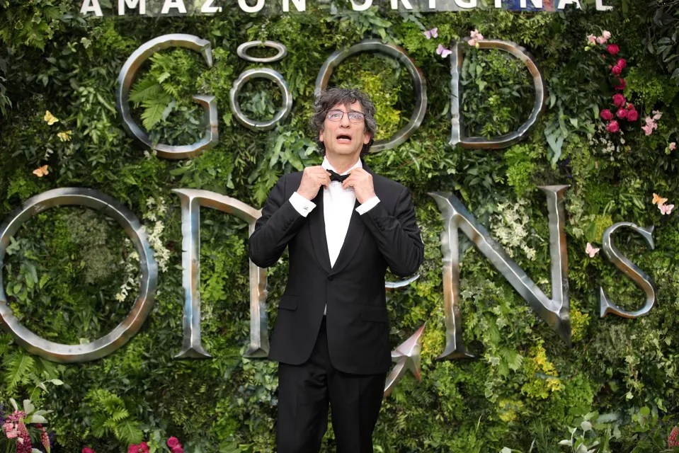 Man adjusting bow tie in front of Good Omens backdrop.