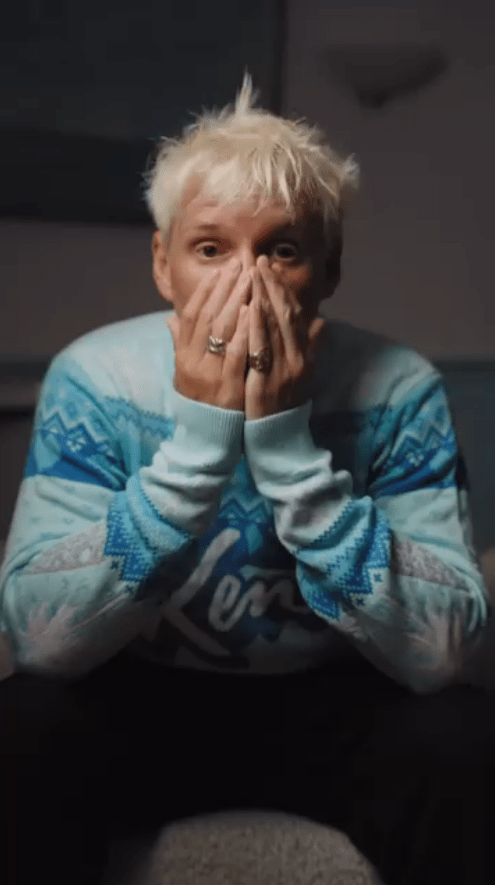 Person with blond hair covering their face with their hands, wearing a blue sweater.