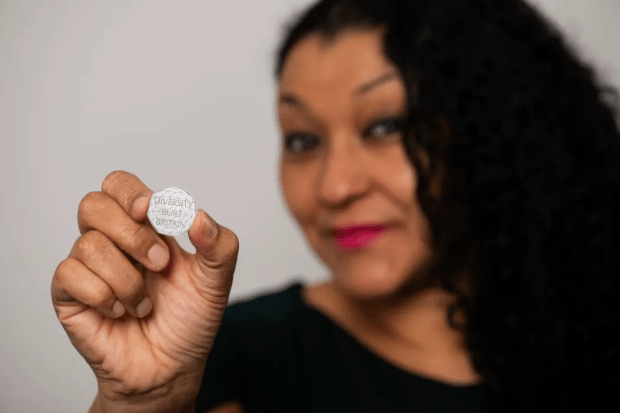 Person holding a coin that says "Diversity Built Britain".