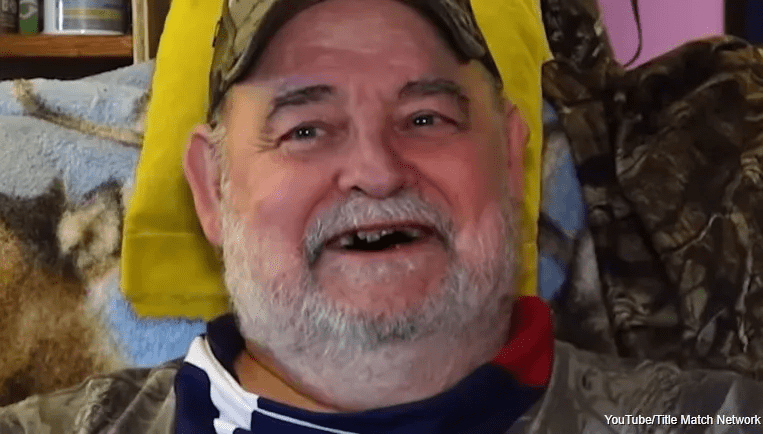 Close-up of a smiling older man with a beard and missing teeth.