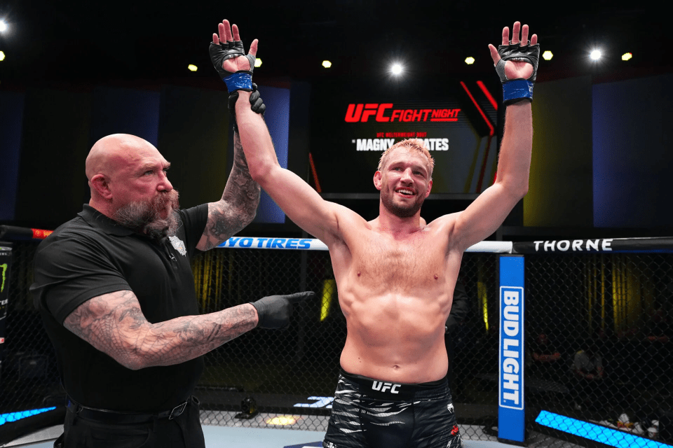 A victorious mixed martial arts fighter raises his arms in the octagon.