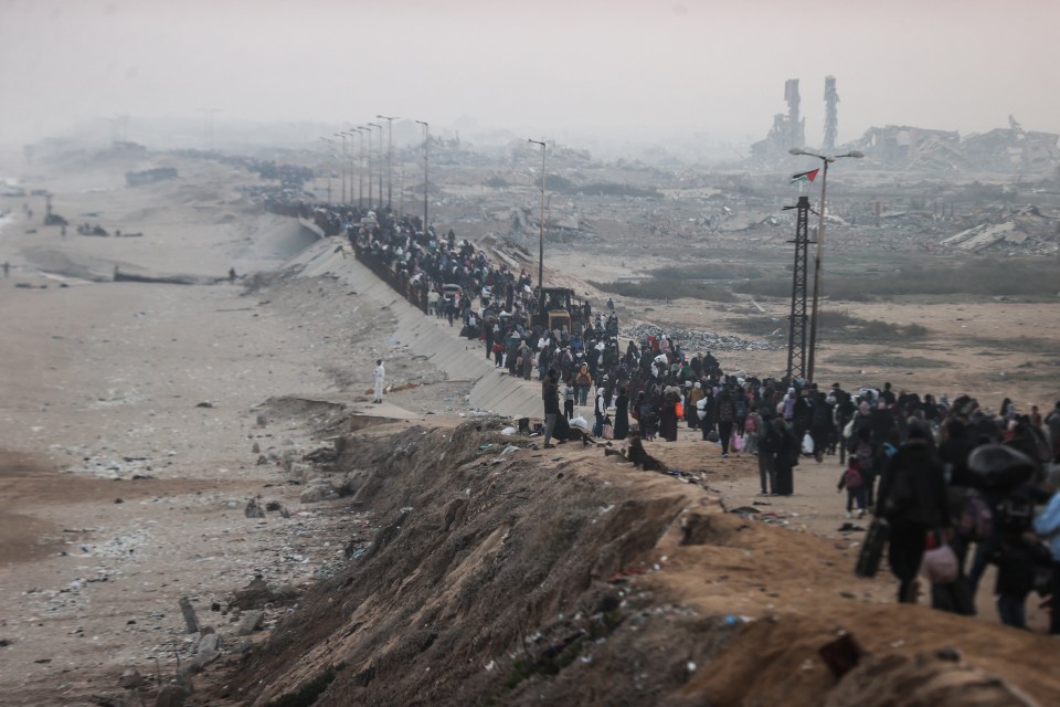 Large group of people walking along a path toward a damaged landscape.