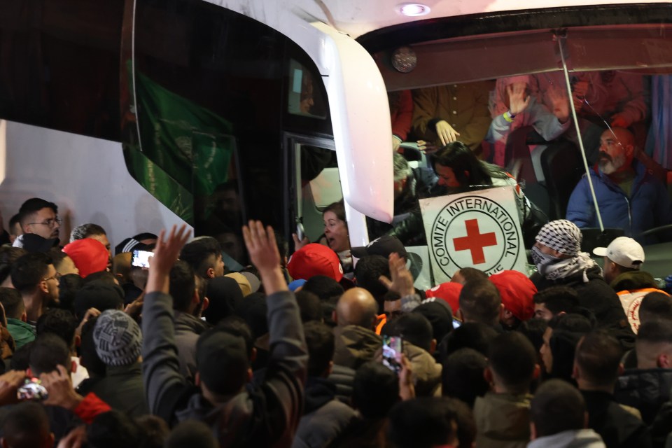 Crowd surrounding a bus with a Red Cross logo.