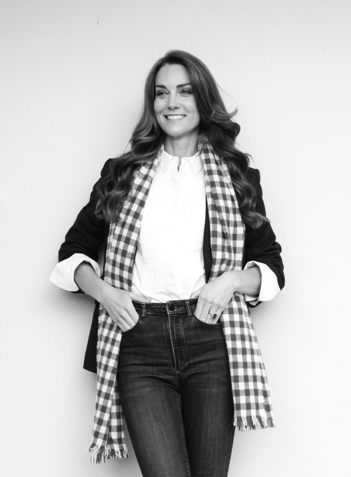 Black and white portrait of a woman wearing a blazer, white shirt, jeans, and a gingham scarf.