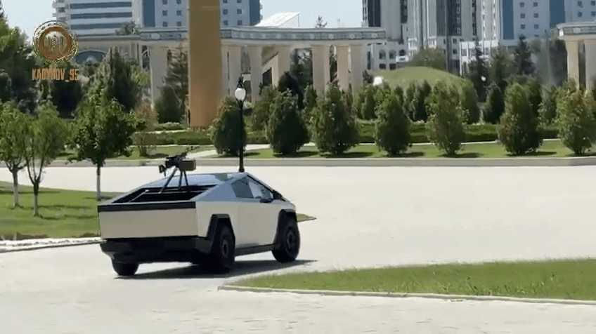 Tesla Cybertruck with mounted machine gun driving on paved road.