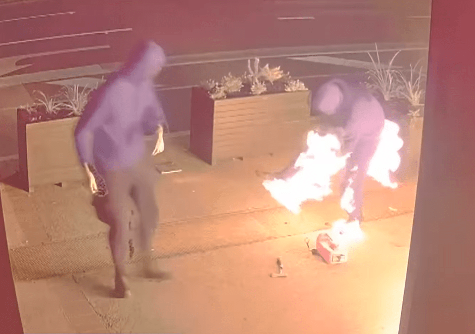 Two hooded figures near a burning object.