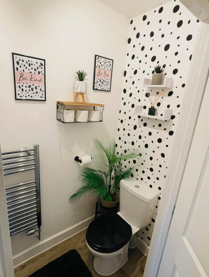 Small bathroom with black and white polka dot wall decor, toilet, and plants.