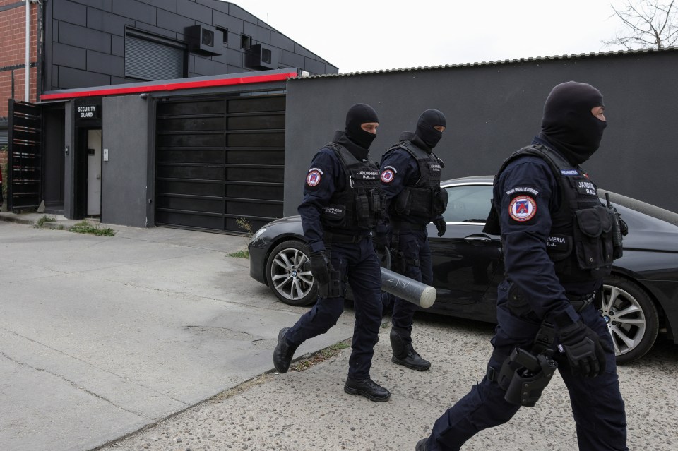 Three police officers in tactical gear walk past a building.