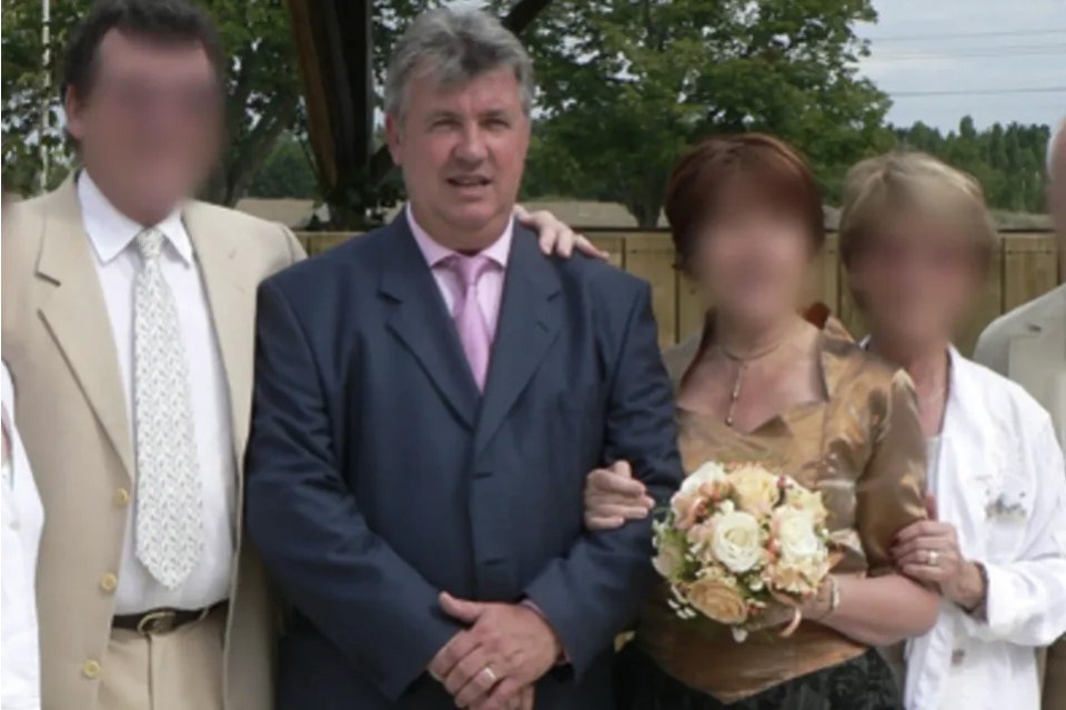 Man in a suit at a wedding with blurred faces of other attendees.