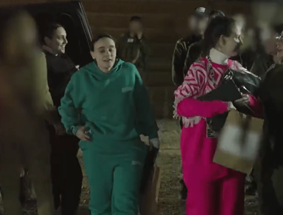 A woman in teal jogging suit and a woman in pink carrying bags exit a vehicle at night.