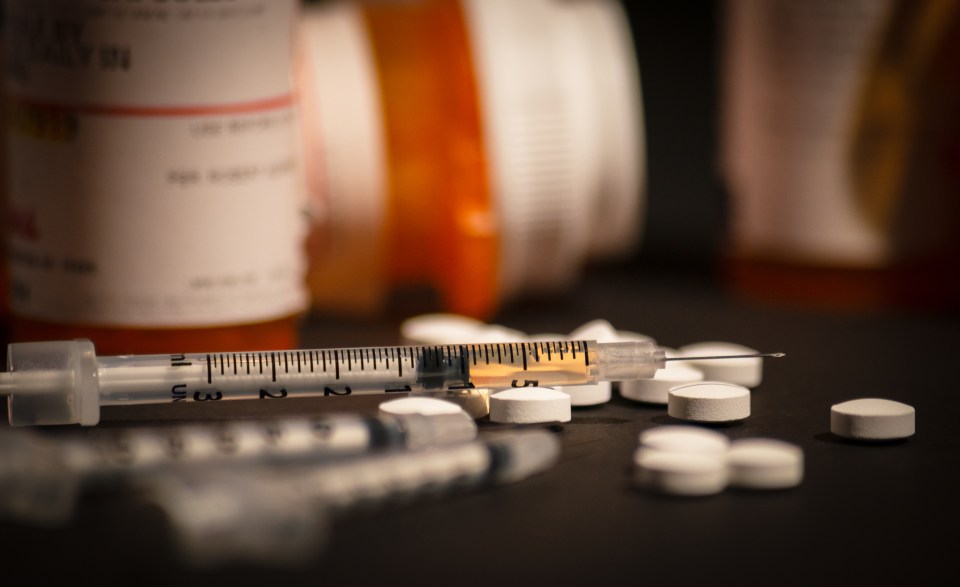 Syringe with injectable drug and scattered pills.