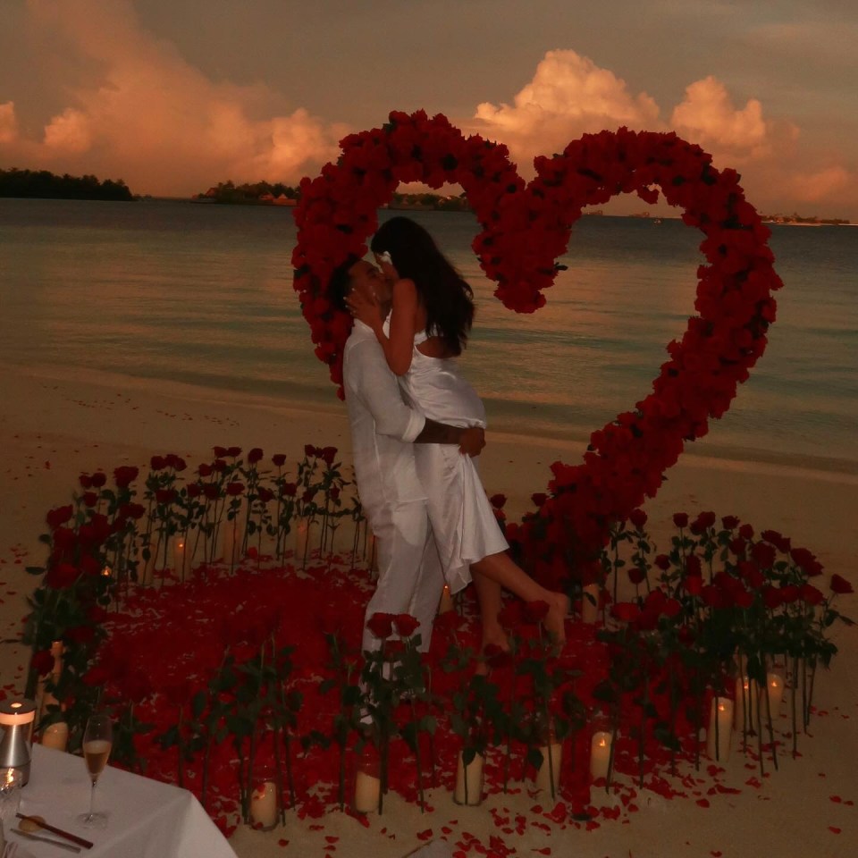 Couple kissing under heart-shaped rose arch on beach.