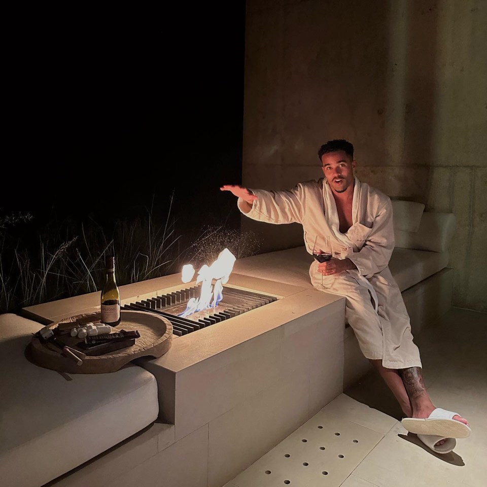 Man in bathrobe roasting marshmallows by a fire pit.