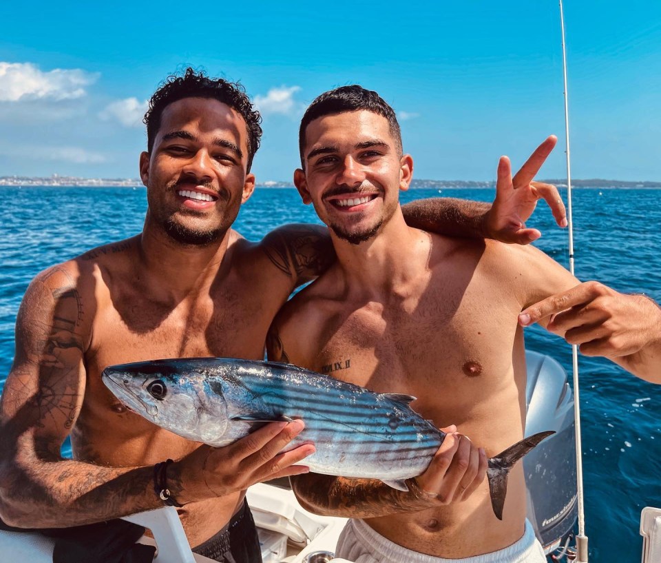 Two shirtless men on a boat holding a fish.