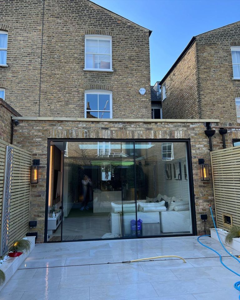 Rear view of a renovated home with a glass wall opening to a patio.