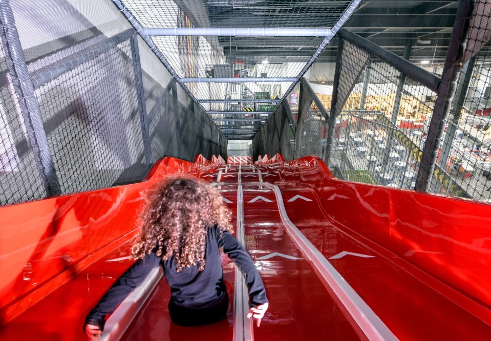 Person going down a long red slide in a large indoor play area.