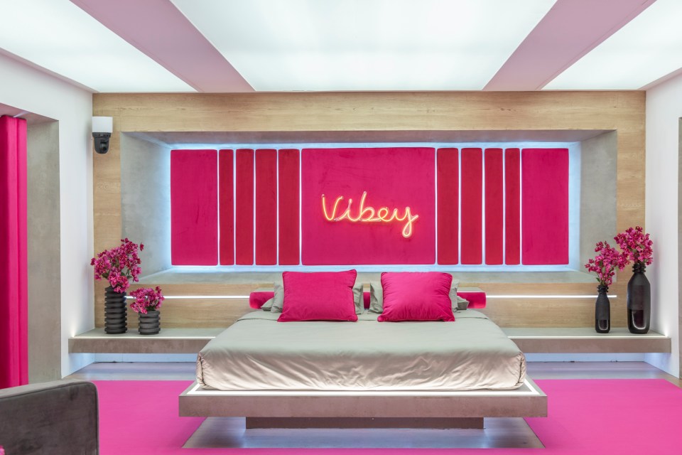 Love Island villa bedroom with pink accents and neon "Vibey" sign.