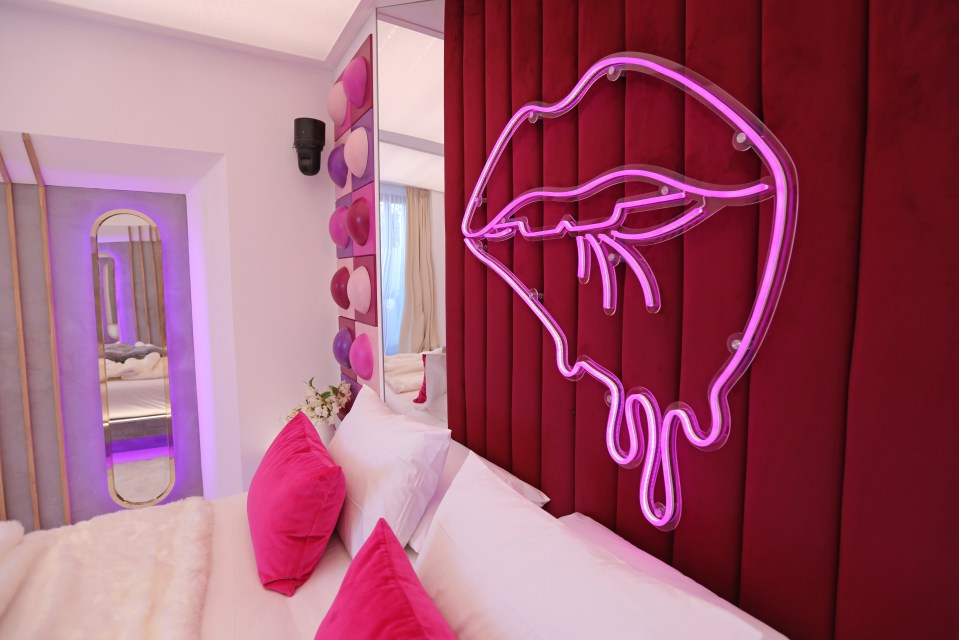 Pink neon lips above a bed with pink pillows.