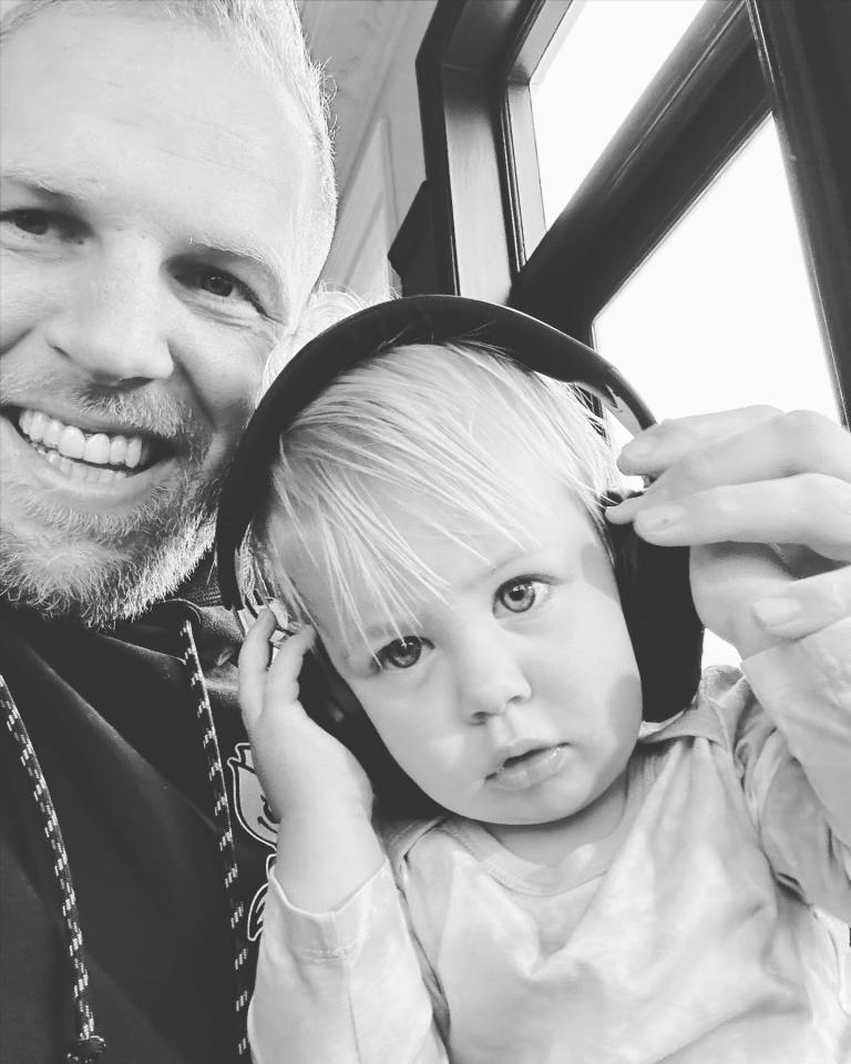 Black and white photo of a man holding a toddler wearing headphones.