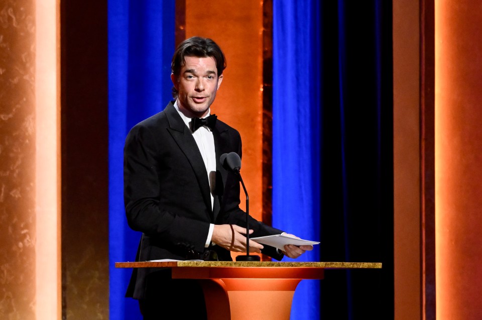 John Mulaney speaking at a podium.