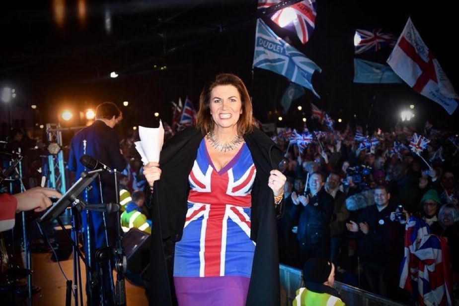 Woman in Union Jack dress addressing a crowd.