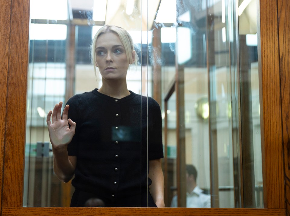 Woman in black shirt viewed through glass partition in courtroom.