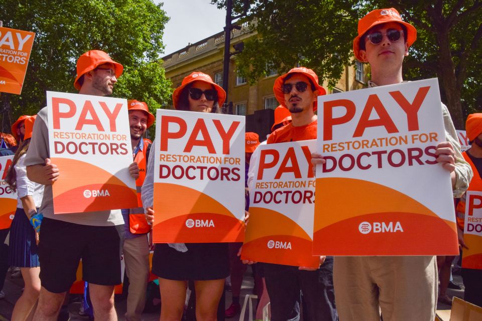 Junior doctors holding signs that read "PAY RESTORATION FOR DOCTORS" at a demonstration.