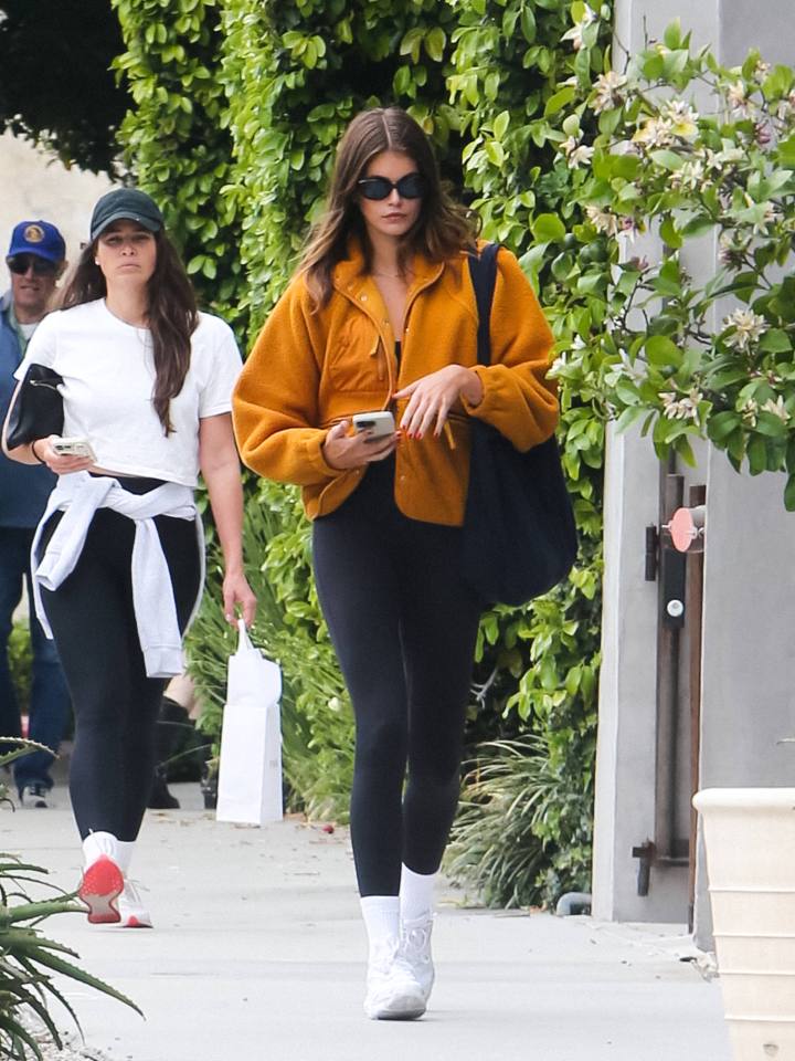 Kaia Gerber walking down the street, looking at her phone.