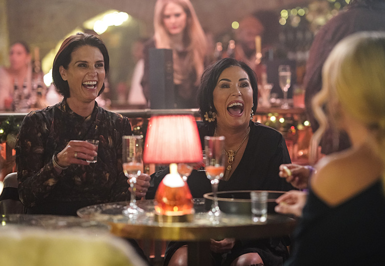 Kat Slater and Sharon Watts laughing together at a table in a bar.