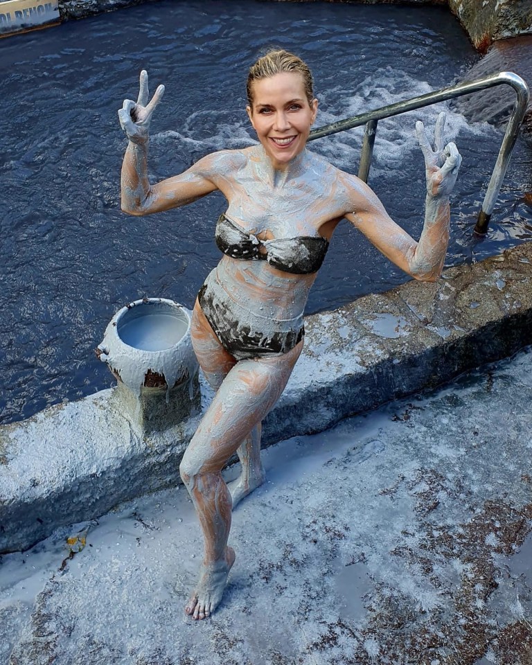 Woman covered in mud giving peace signs in a pool.