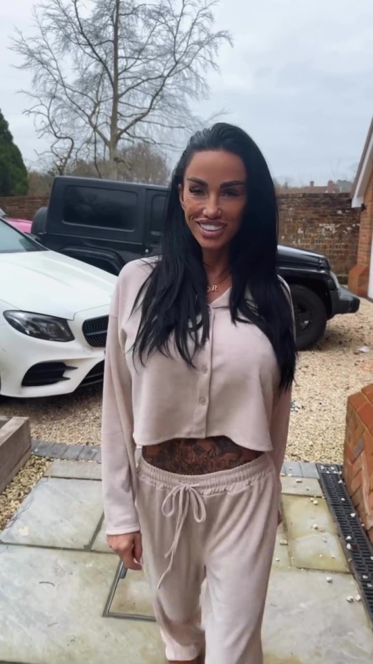 Katie Price showing off her stomach tattoo while wearing a beige tracksuit.