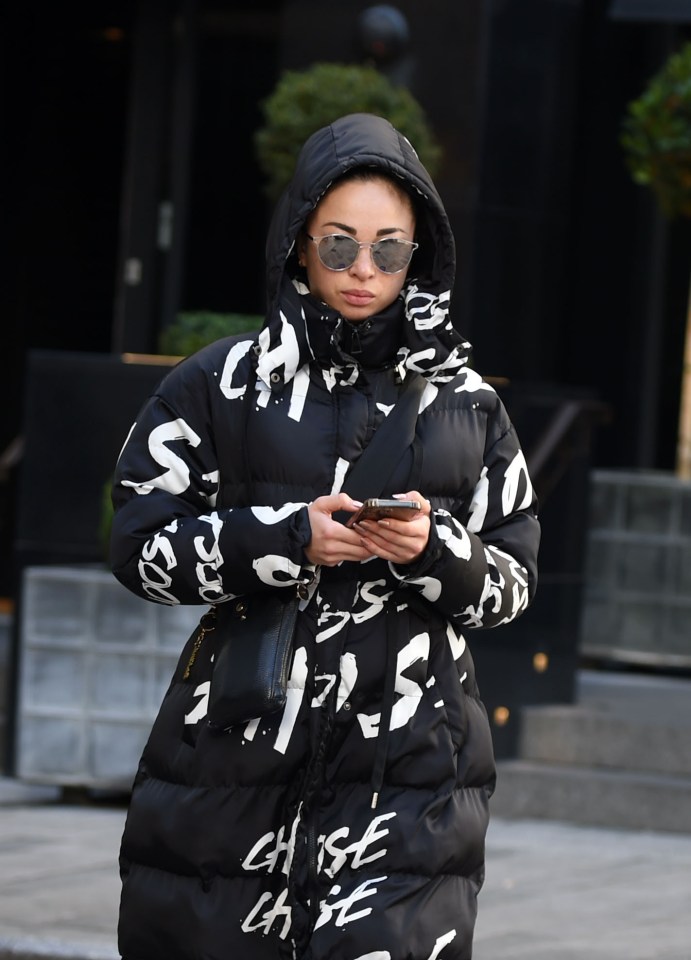 Katya Jones using a phone while wearing a black and white patterned puffer jacket and sunglasses.