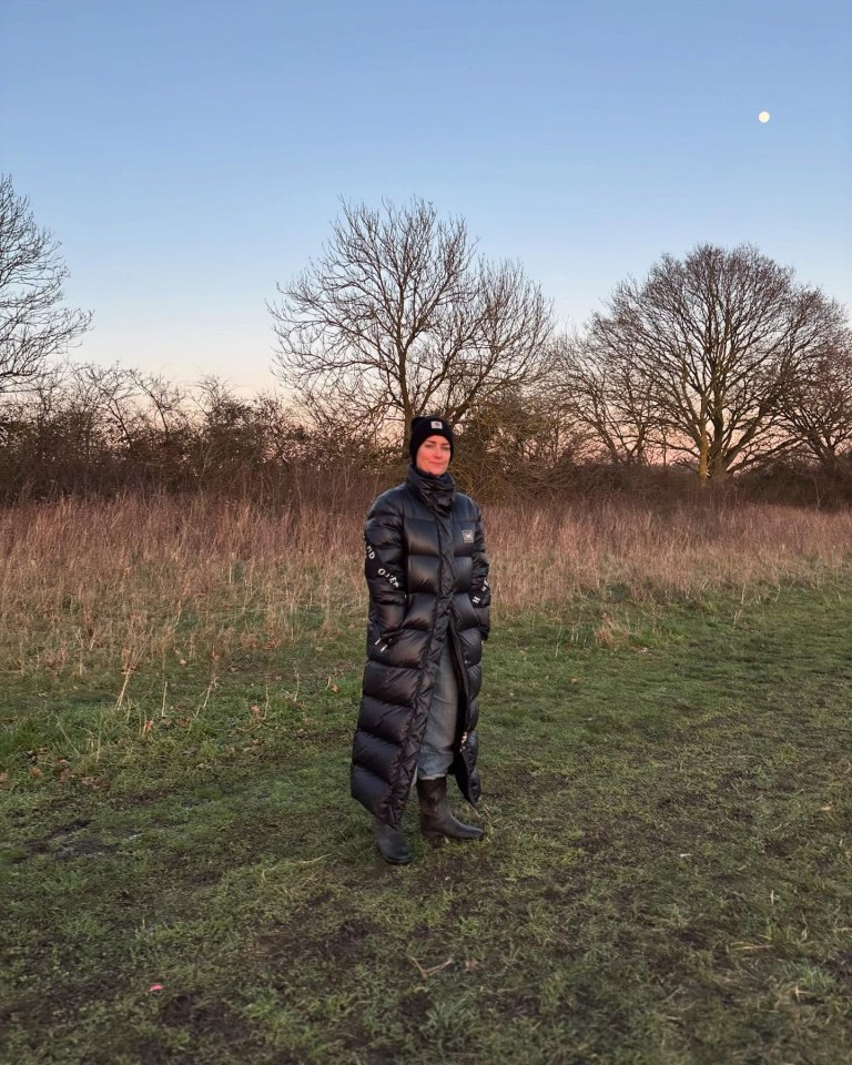 Woman in long black puffer coat standing in a field.