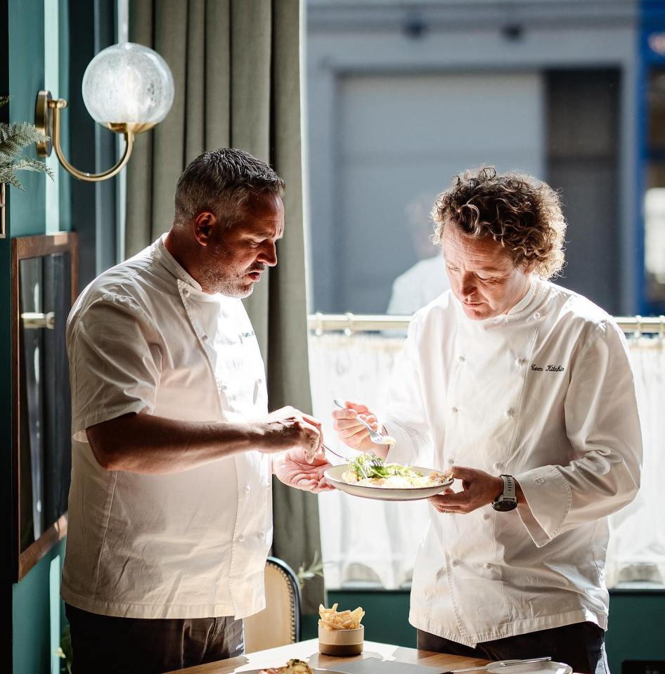 Two chefs in white jackets examining a plated dish.