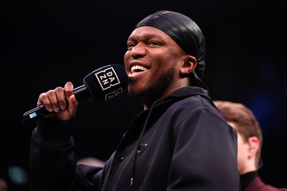 KSI speaking into a microphone at a boxing event announcement.