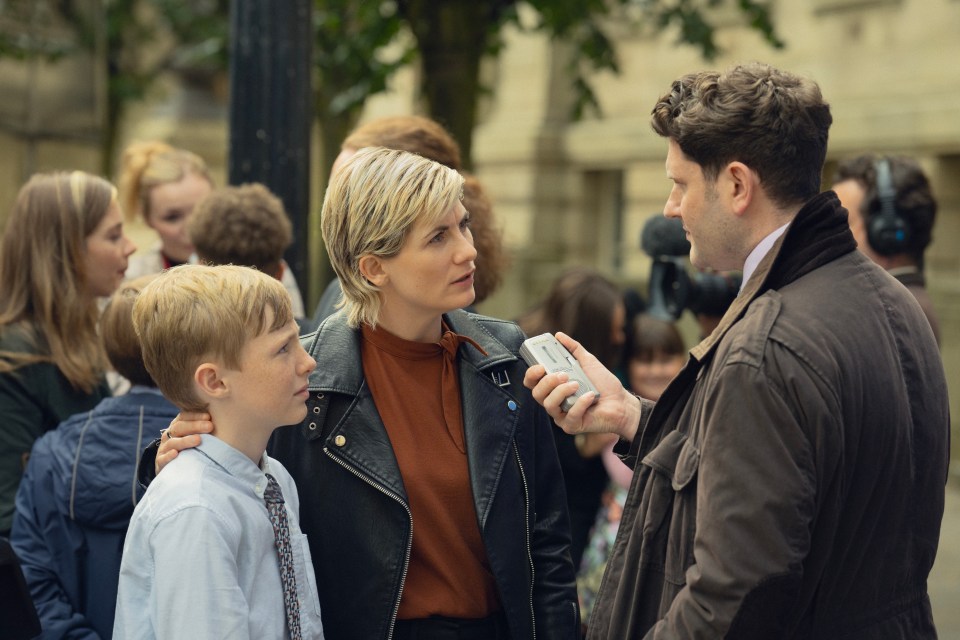 A reporter interviews a woman and child amidst a crowd.