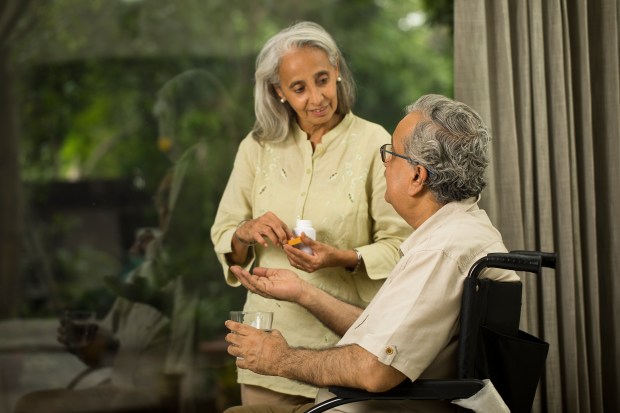 A woman gives her husband, who is in a wheelchair, his medicine.