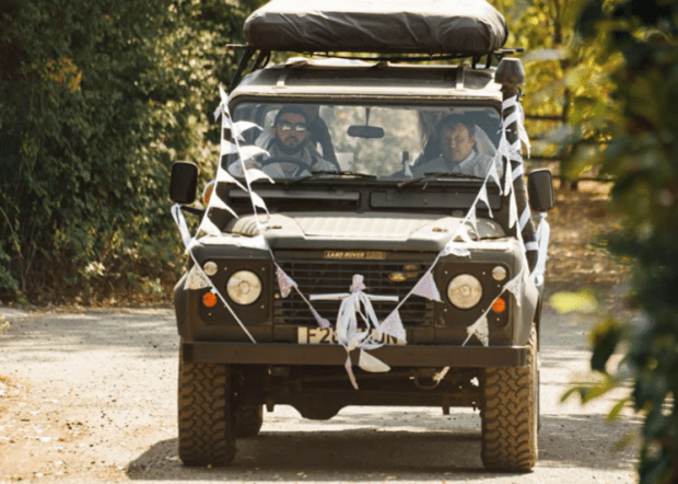 Land Rover Defender decorated for a wedding, driven by two people.