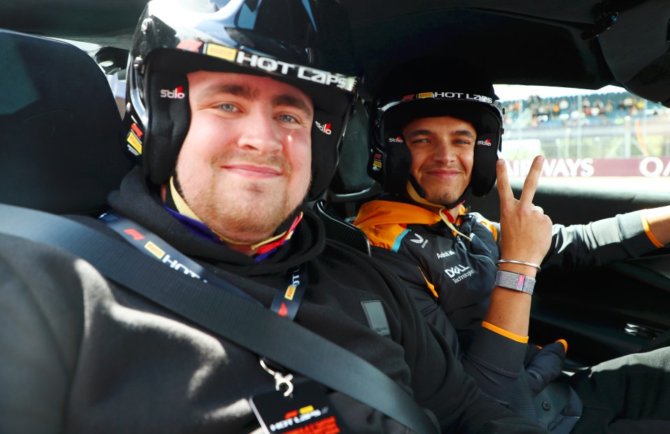 Lando Norris and another person in a race car, giving a peace sign.