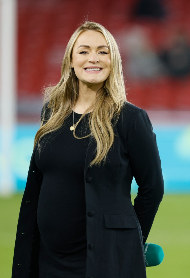 Laura Woods, a pregnant TV sports presenter, smiles on a soccer field.