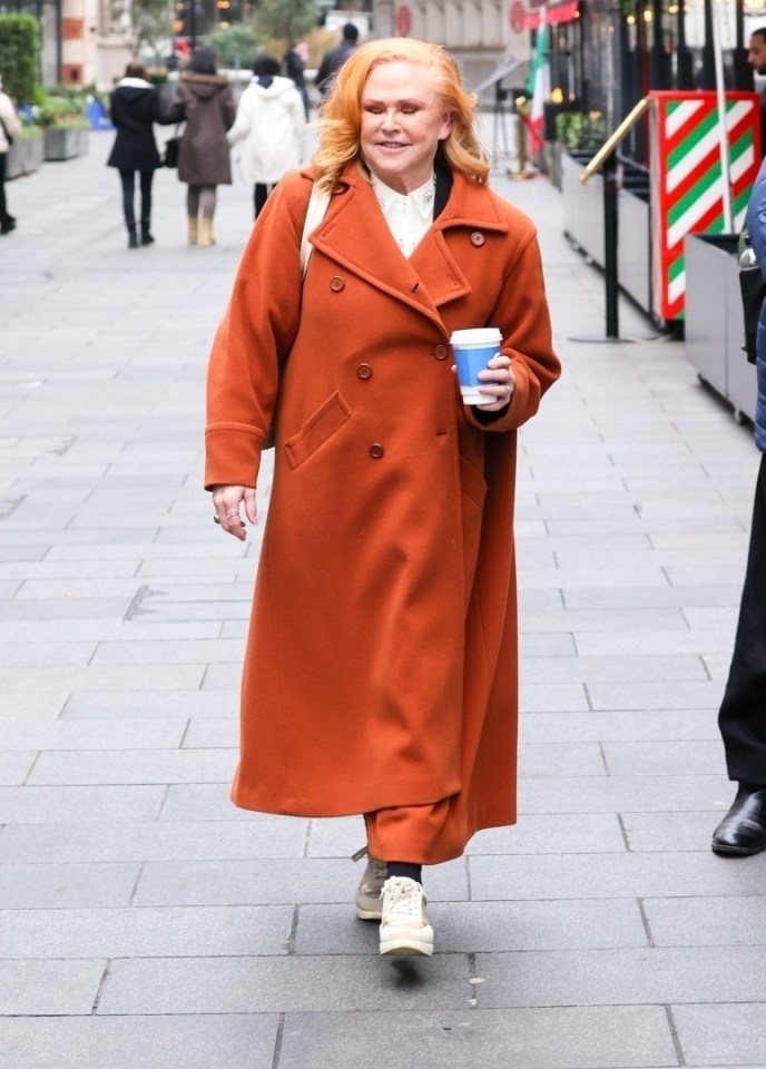 Carol Decker, lead singer of the 80s pop band T'Pau, walking down a street while holding a coffee cup.