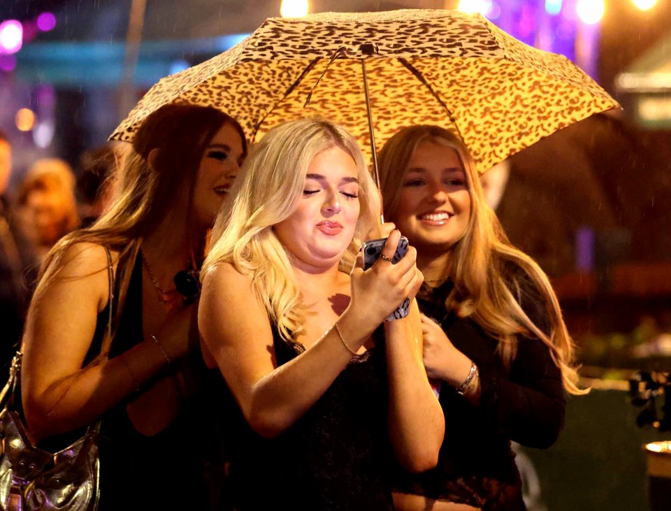 A young woman checks her phone as she shares an umbrella