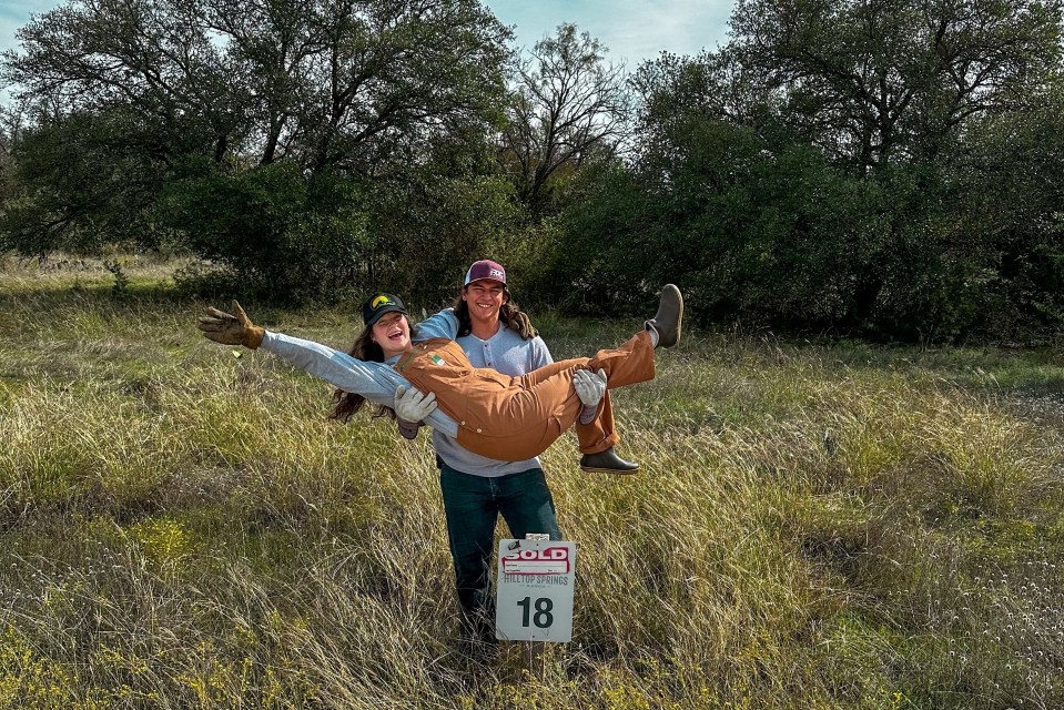 A man playfully lifts a woman in the air on a plot of land marked as sold.