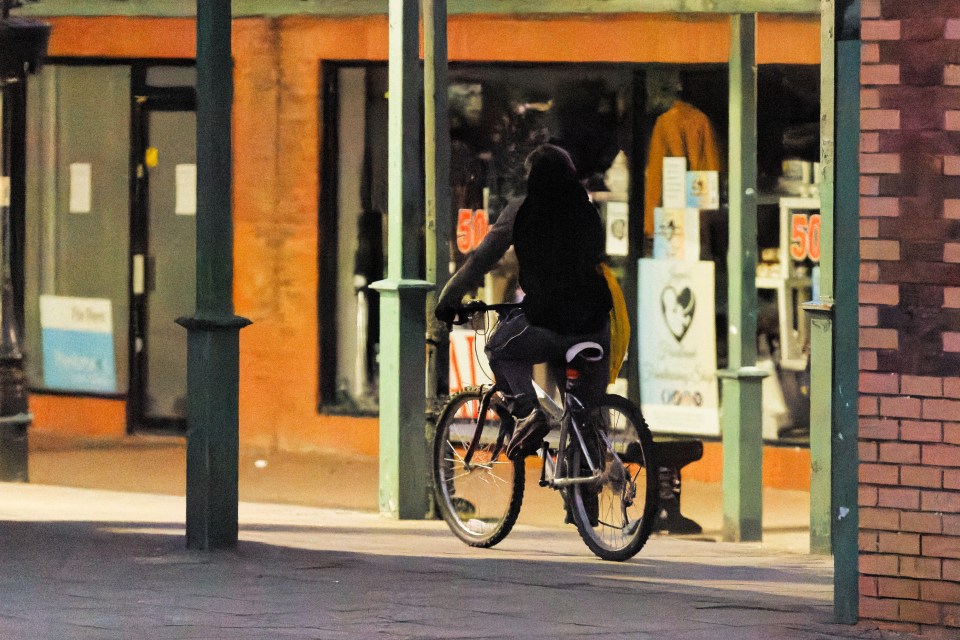 Person riding a bicycle at night in a town center.