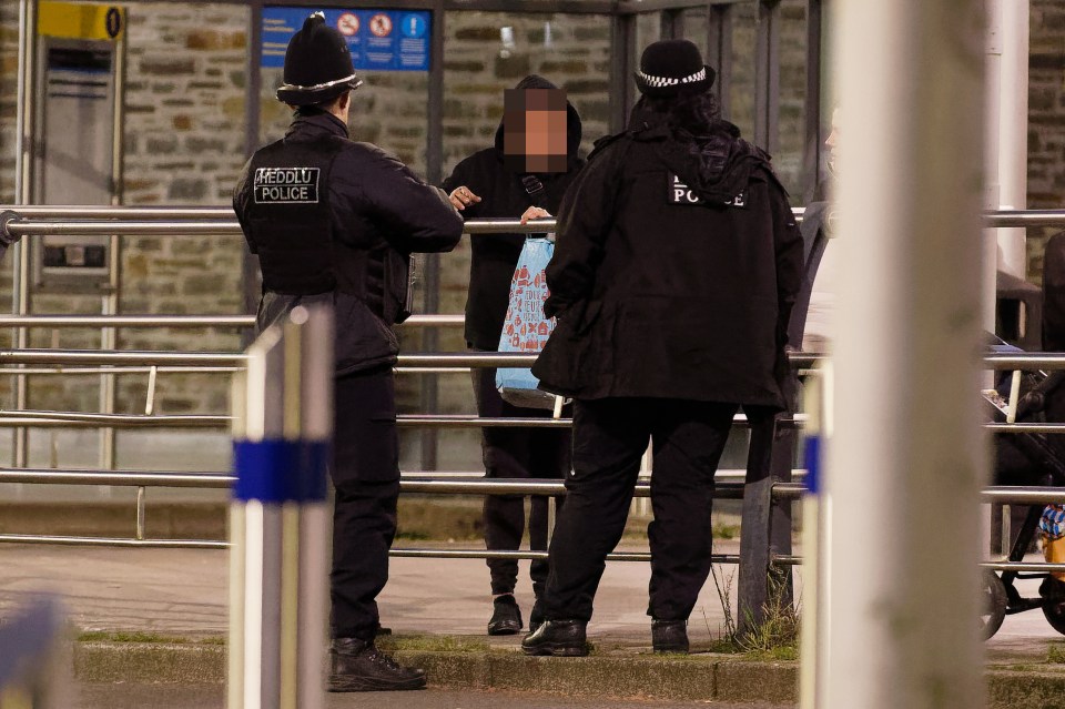 Two police officers speaking with a person at a bus station.