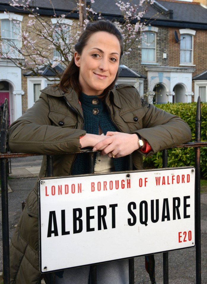 Sonia, an Eastenders character, standing by an Albert Square sign.