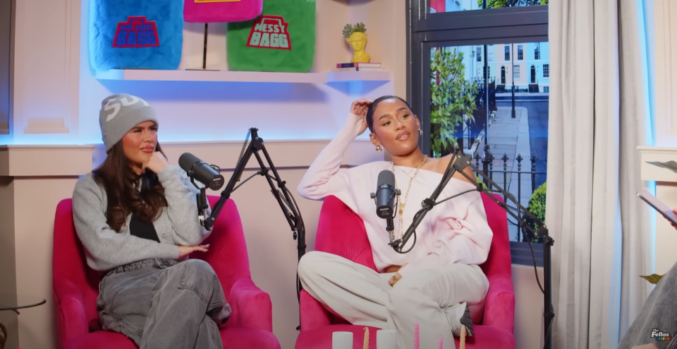 Two women sitting in pink chairs during a podcast interview.