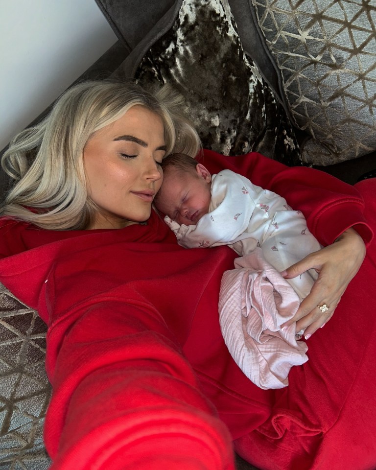 Woman in red sweatshirt cuddling sleeping newborn baby.