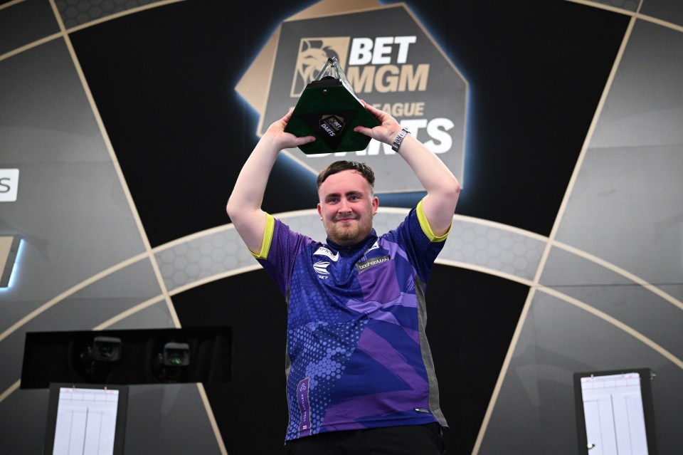 Luke Littler holding up a Premier League Darts trophy.